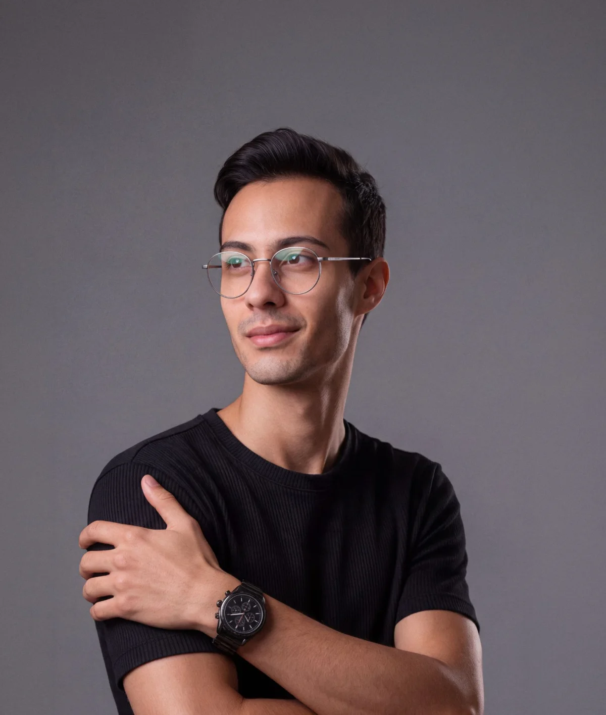 Retrato de Fabio Correa sobre fundo cinza, de óculos redondos e camiseta preta, braços cruzados, olhando para o lado.